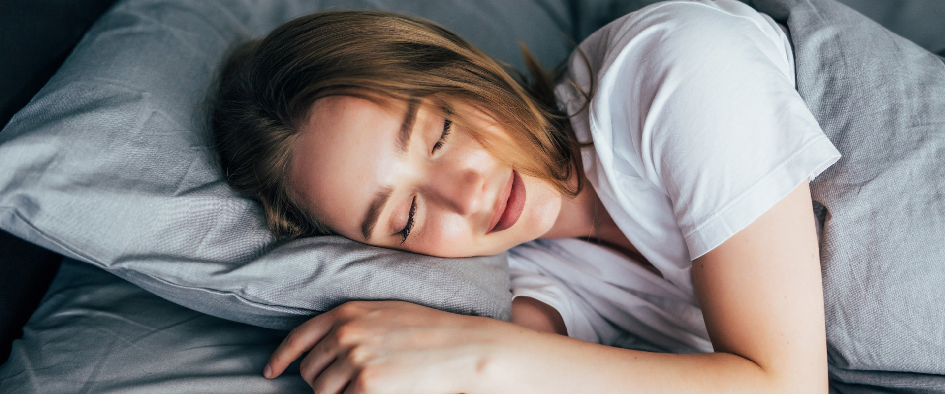 Frau schläft in einem Bett mit grauer Bettwäsche